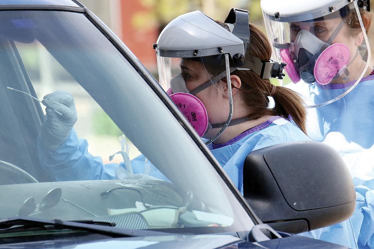 Nurse reaches into the window of a car to conduct COVID-19 test
