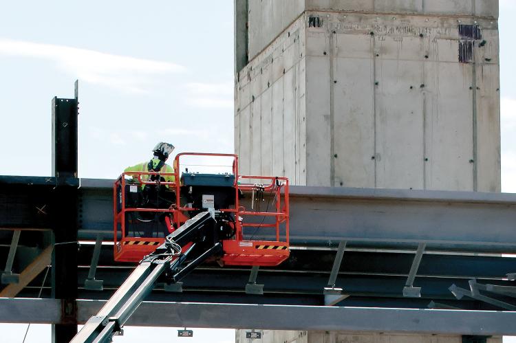 A construction worker uses a crane to work on a piece of steel