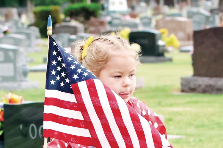 Colette Burns puts a flag on the grave of a veteran