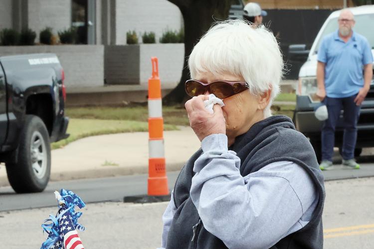 A woman holding an American flag wipes tears from her eyes