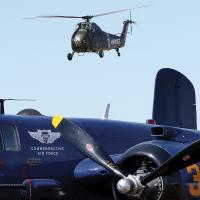 A pair of Vietnam-era helicopters fly over the B-25 bomber Devil Dog