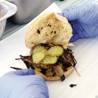 A worker stacks pickles on a burger during this year’s Burger Day