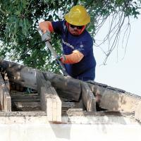 A worker removes decades-old roof shingles