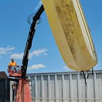 A worker uses a crane to lift a boat into a dumpster