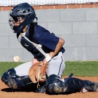 Austin Castanon uses his chest protector to clock a low throw into the plate