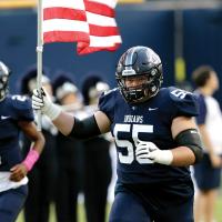 Rafe Goucher carries an American flag onto the field at Memorial Stadium
