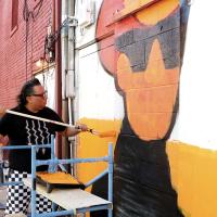 Micah Wesley uses a small roller to smooth out the orange paint