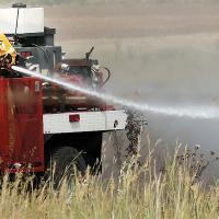 A firefighter sprays water on a patch of smoking grass
