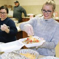 Maygan Mitchell sprinkles cheese on a taco as Jamie Hoffman looks on