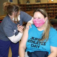 Katie Scheirer squints as Nicki Cerne sticks a needle into her arm