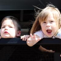 Two children look at the crowd out a bus window