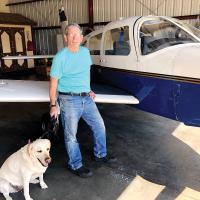 Ken Larcher and his dog Daisy are shown next to the plane he uses to teach
