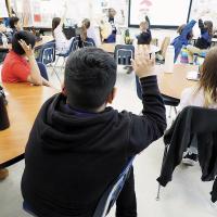 Students raise their hands in a fourth-grade classroom