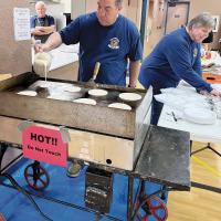Jason Pennington cooking pancakes while Mary Wright helps serve