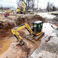 Construction workers watch as a backhoe is used to move dirt