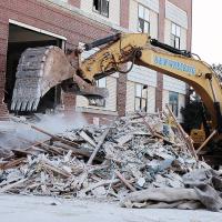 A large excavator creates a cloud of dust while moving debris away
