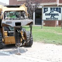 A worker uses a jackhammer attachment to break up the old sidewalk