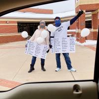 Vera Puls and Russ Wells hold signs greeting students