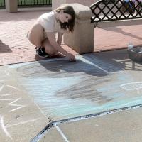 Malone Cowan uses black chalk to highlight a tornado on the sidewalk
