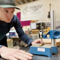 Tyler Willoughby measures a wraparound tailpiece made for an electric guitar