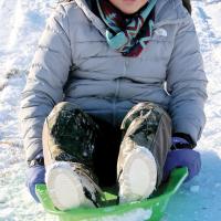 Violet Roman Nose uses a plastic sled to slide down a hill