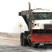 A truck equipped with a snow plow fans out a layer of sand