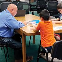 Craig McVay uses crayons to make a drawing along with Jovanni and Benjamin Quiroz