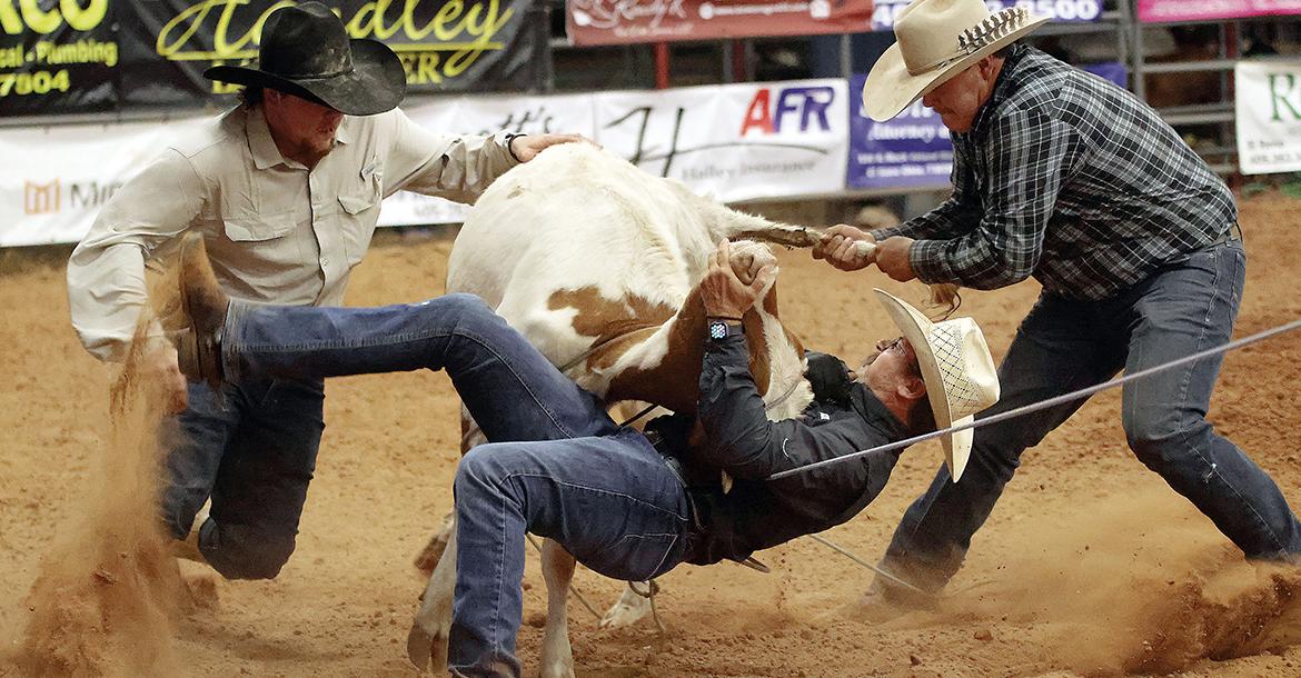 Ray Cambron (center) tries to flip a calf as Rope Jones (left) and Dalton Wykoff come to his aid_slideshow