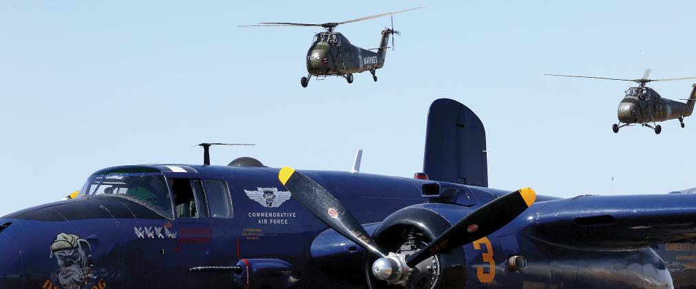 A pair of Vietnam-era helicopters fly over the B-25 bomber Devil Dog