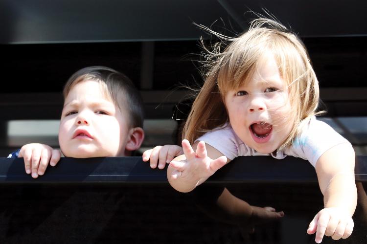 Two children look at the crowd out a bus window